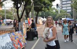 Mulher segura cachorro na Praça da Savassi. Ao lado dela, há quadros pintados