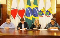 Foto mostra a secretária de Política Urbana, Maria Caldas, falando ao microfone. Ao fundo, as bandeiras de MG, BH e do Brasil.